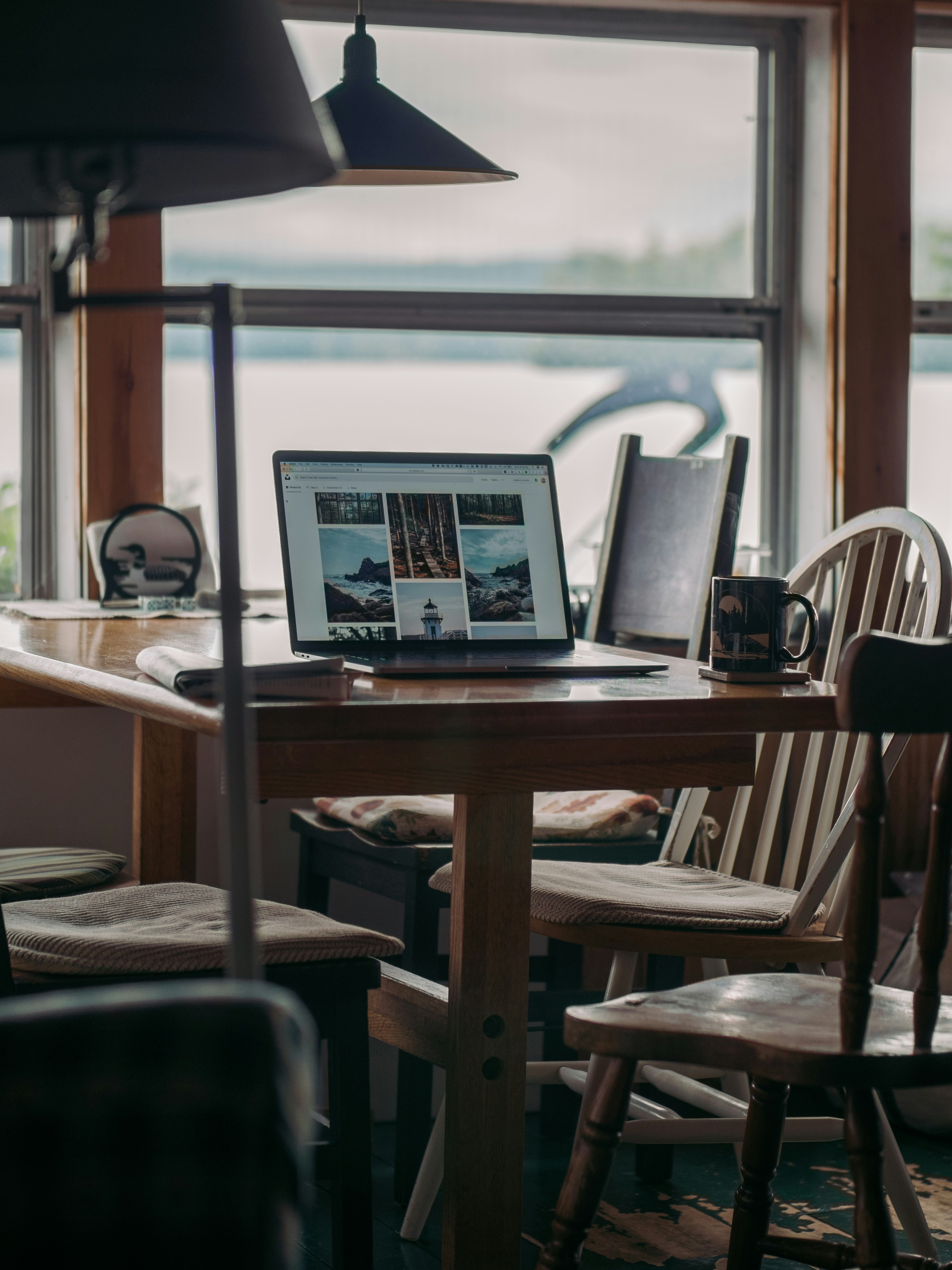 A laptop and coffee on a wooden table by a window overlooking water
